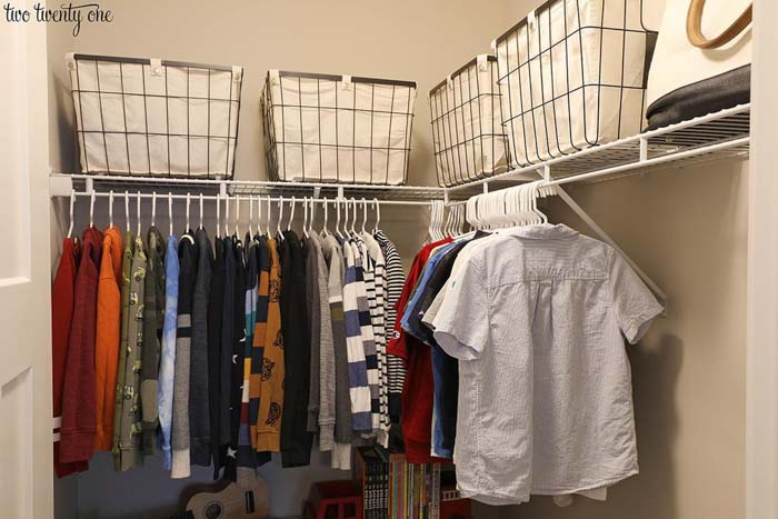 closet with baskets on top shelves and clothing hung on racks