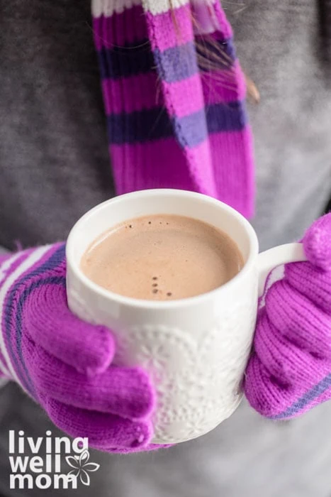 person with scarf and gloves holding a mug of cocoa