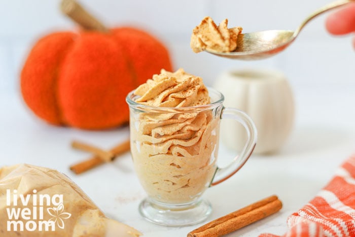 A spoonful of pumpkin whipped cream being scooped from a cup.