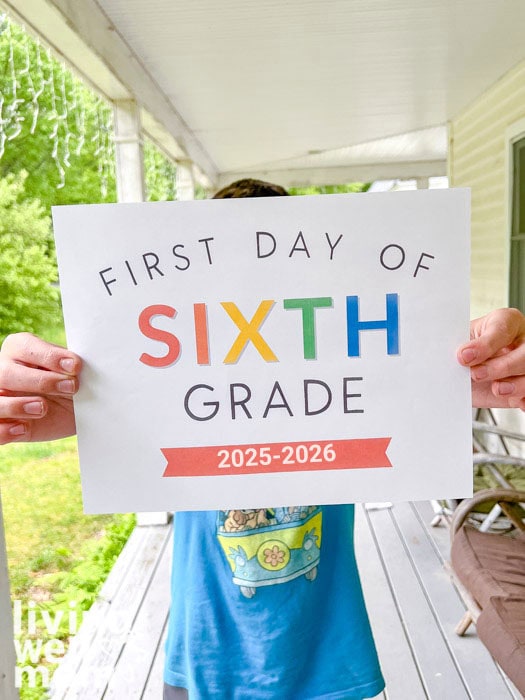 boy in blue shirt holding up free 1st day of school sign for 2025 school year