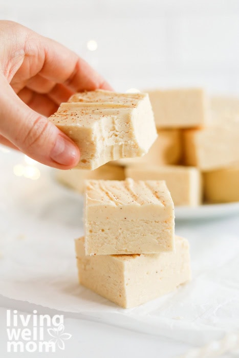 Hand grabbing a square of eggnog fudge from a plate.