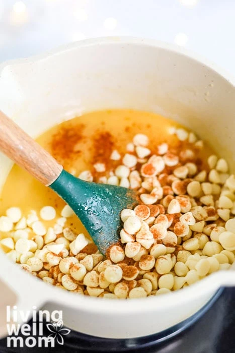 White chocolate chips and nutmeg being stirred into a saucepan