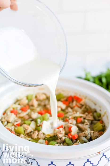 Pouring cream into creamy chicken and wild rice soup in the slow cooker