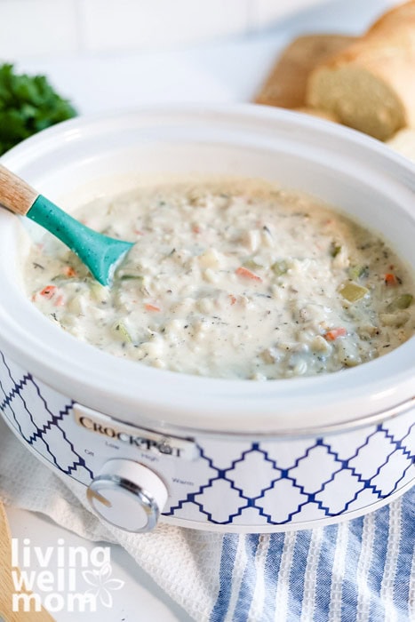 A blue and white crockpot filled with creamy chicken and wild rice soup with bread in background