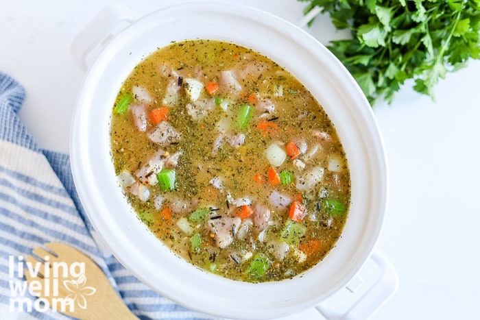 Chicken broth being added into a crockpot filled with vegetables and wild rice
