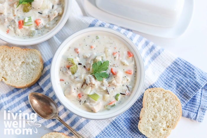 Overhead shot of creamy wild rice soup in 2 bowls alongside crusty french bread