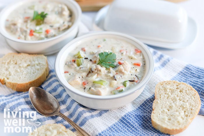 Slow cooker creamy wild rice soup in 2 bowls alongside crusty french bread