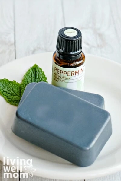 Homemade charcoal soap bars on a dish next to peppermint oil bottle