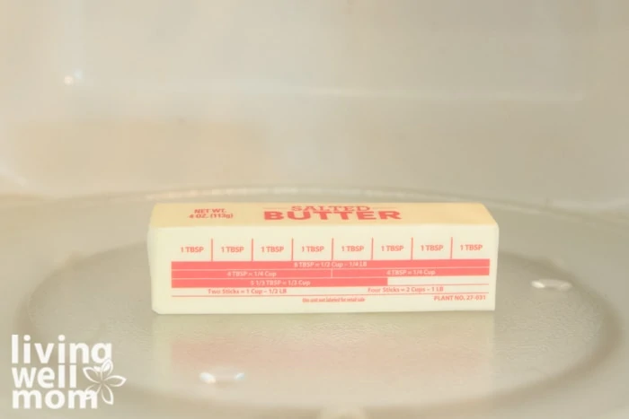 A stick of butter, still in the wrapper, on the tray inside of a microwave. 