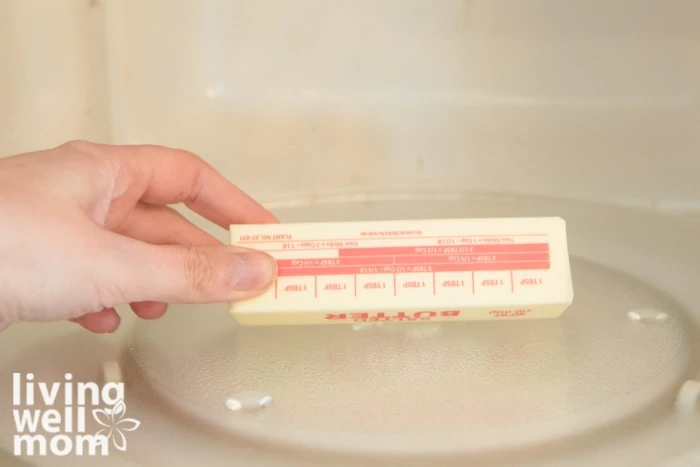 A hand flipping over a wrapped stick of butter in the microwave. 