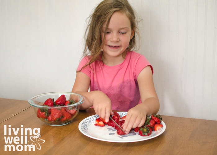 child cutting strawberries for a rainbow fruit bowl