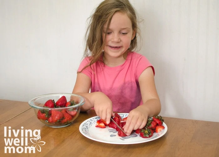 child cutting strawberries for a rainbow fruit bowl