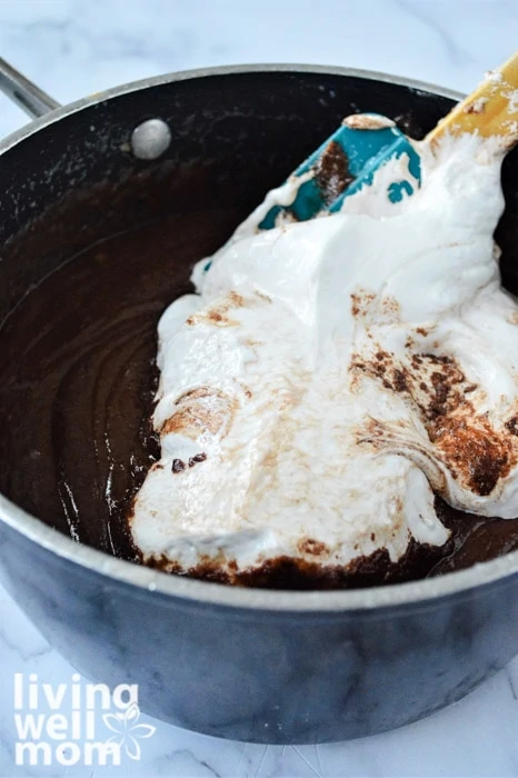 Adding marshmallow fluff to a pot of melted fudge