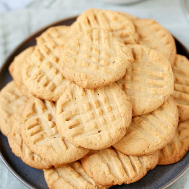 Pile of gluten free peanut butter cookies with bowl of peanut butter in the background.