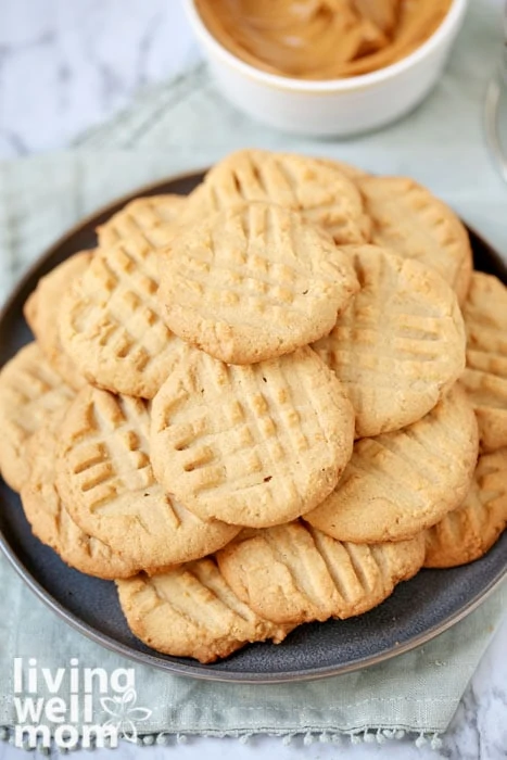 Pile of gluten free peanut butter cookies with bowl of peanut butter in the background.