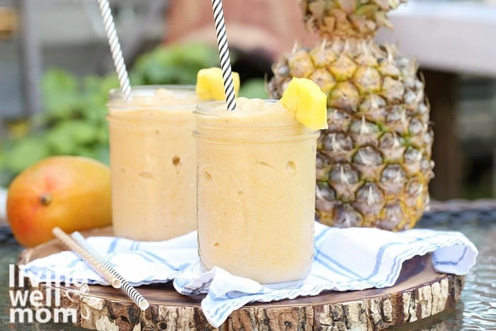 2 mango pineapple smoothies on a wood round