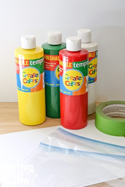 Bottles of finger paint, with paper, ziplock bags and painters tape on a table. 