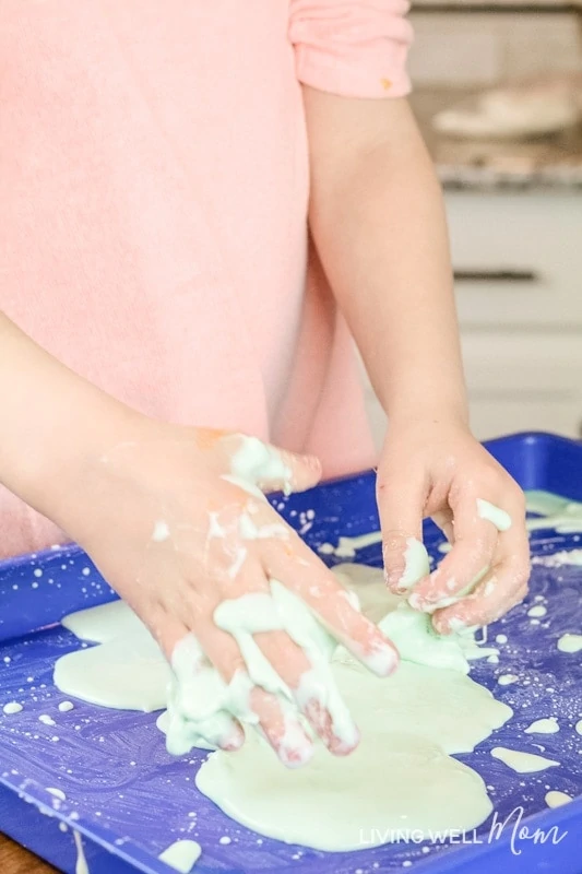 A kid playing with sticky, green oobleck slime on a blue tray. 