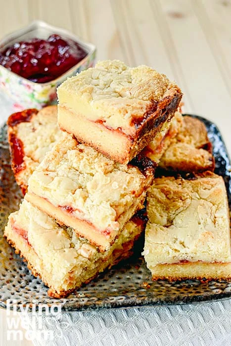 pile of white chocolate raspberry bars with raspberry jam in background