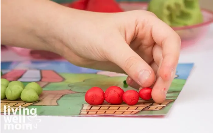 A person placing playdough apples into a basket on an activity mat. 