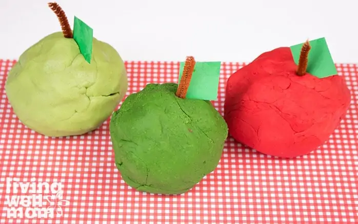 Large balls of red and green playdough apples, with a construction paper leaf and pipecleaner stem.