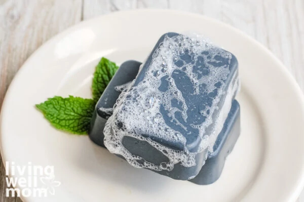 sudsy homemade charcoal soap bar on a white plate with mint leaves