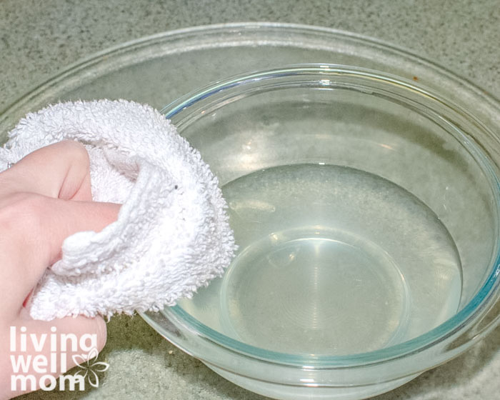 Woman wiping down a microwave with a bowl of cleaning solution