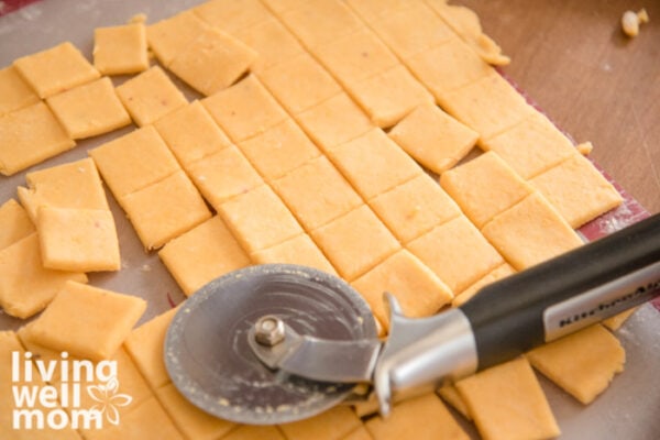 Using a pizza cutter to cut homemade crackers into small squares