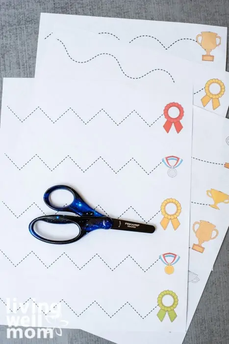 A fair of black and blue Fiskars brand scissors for kids, on a printed cutting practice sheet.