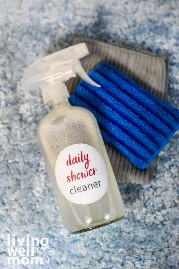 clear spray bottle with daily shower cleaner, blue sponge, and grey towel 