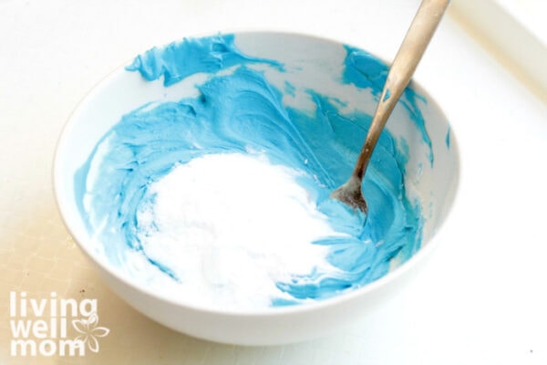 Adding baking soda to a bowl of blue slime base