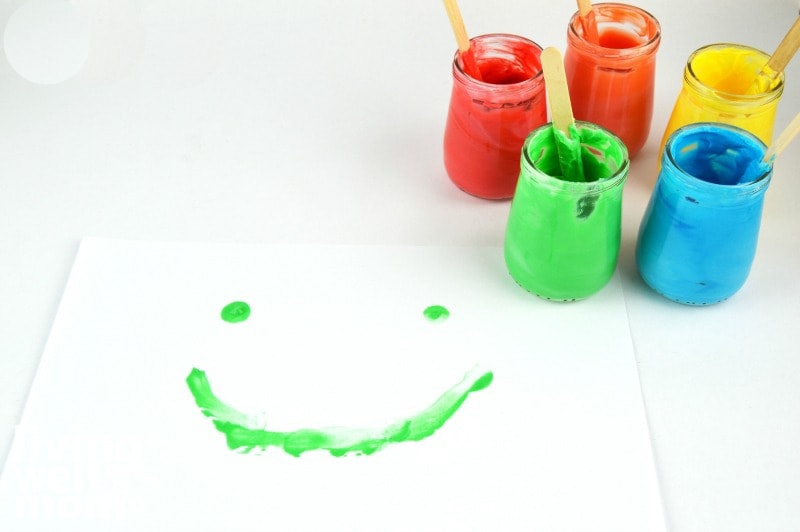 jars of edible finger paint with a green smiley face painted on a piece of paper