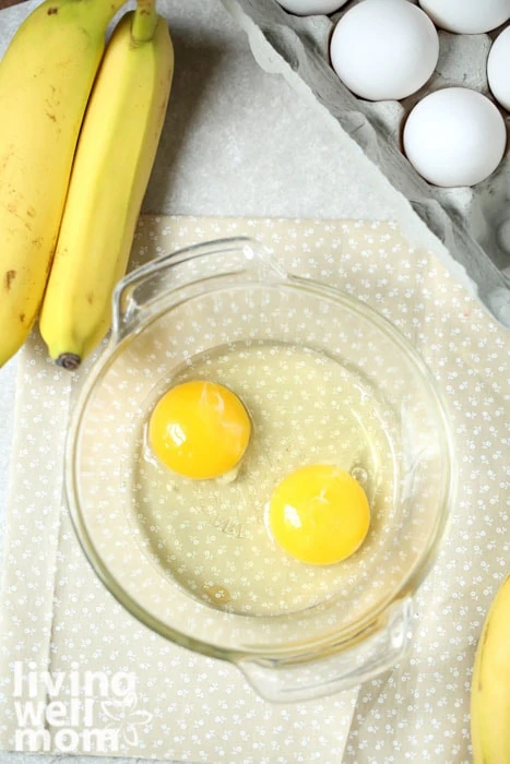 Cracked eggs in a bowl with bananas next to it