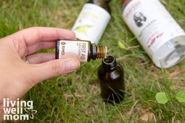 adding first aid essential oil blend to glass bottle on grass