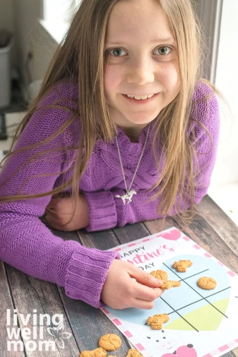 Young girl in purple sweater playing a Valentine's Day tic tack toe game with cookies.