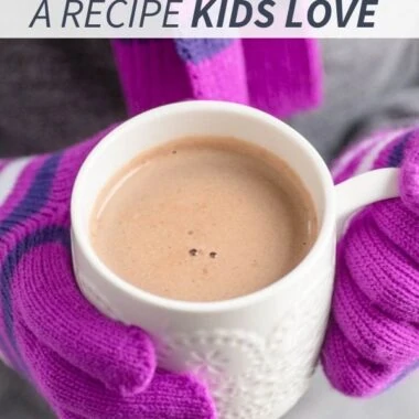 girl in purple gloves holding a white mug with hot cocoa in it