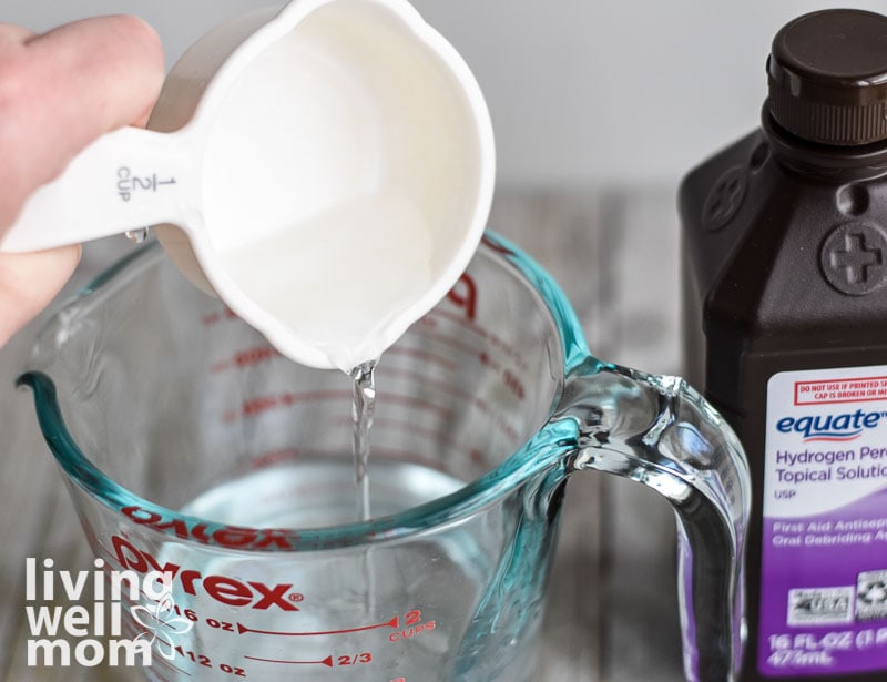 pouring hydrogen peroxide into a glass measuring cup for diy cleaner recipe