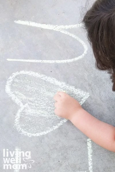 Dark haired child coloring in a heart on a sidewalk with diy chalk