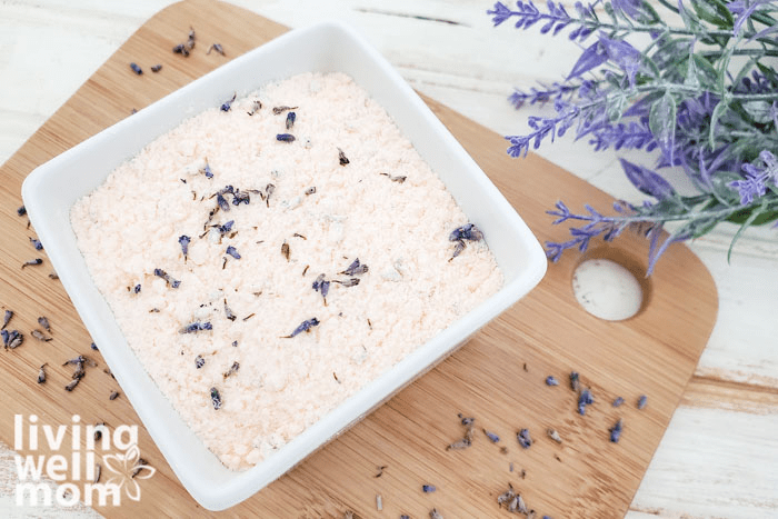 DIY bath soak on a cutting board atop of a surface, with a bouquet of lavender to the side. 
