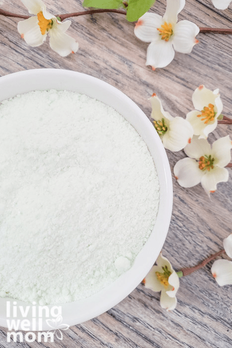 Scented homemade bath salts in a white bowl next to faux flowers. 