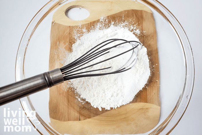 A whisk sitting in a bowl of DIY coconut bath bomb mixture. 