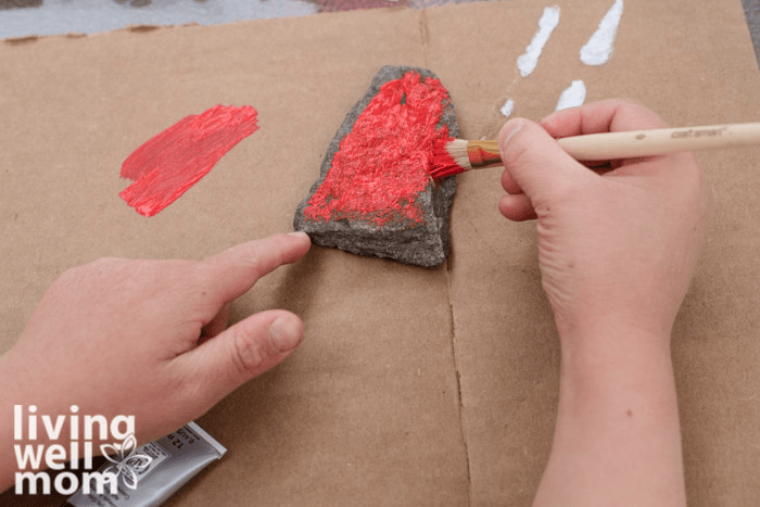 A child painting a small rock with red acrylic paint. 