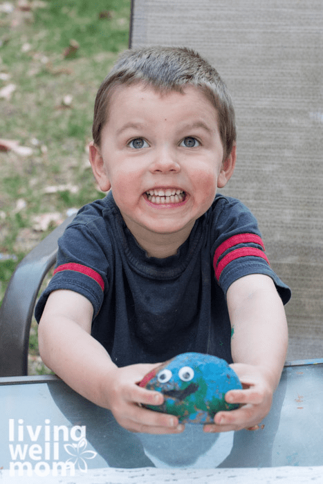 A boy proudly showing his pet rock painted with blue, green and red acrylics.