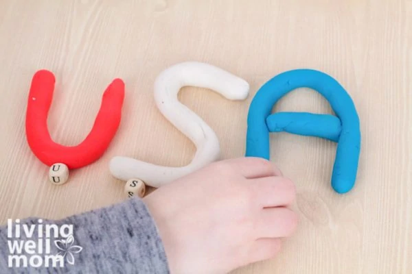 Child spelling USA with red, white, and blue playdough