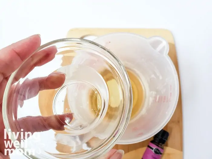 A small bowl of almond oil about to be poured into a measuring cup of homemade lotion bar ingredients.