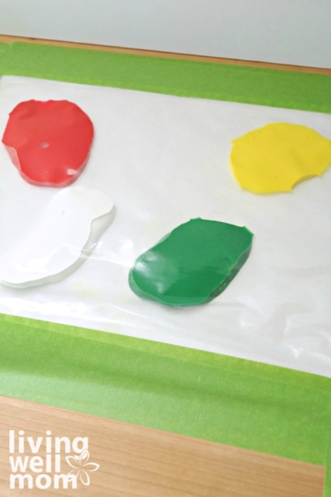 Large drops of red, green, yellow and white finger paint inside of a ziplock bag. 