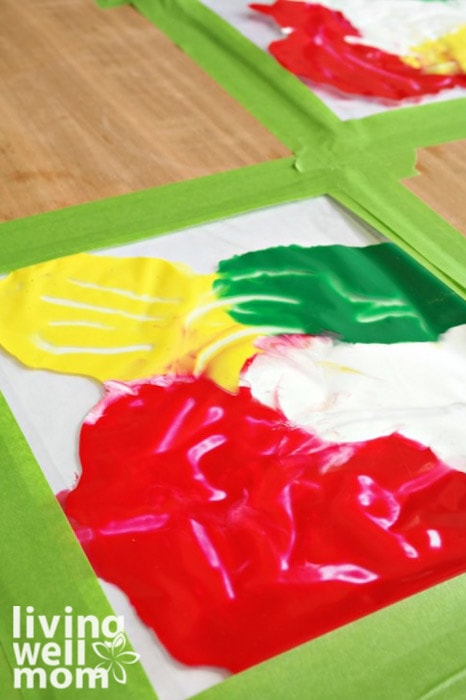 Washable paints spread around a piece of art paper inside of plastic, with toddler finger prints and tracks clearly visible. 