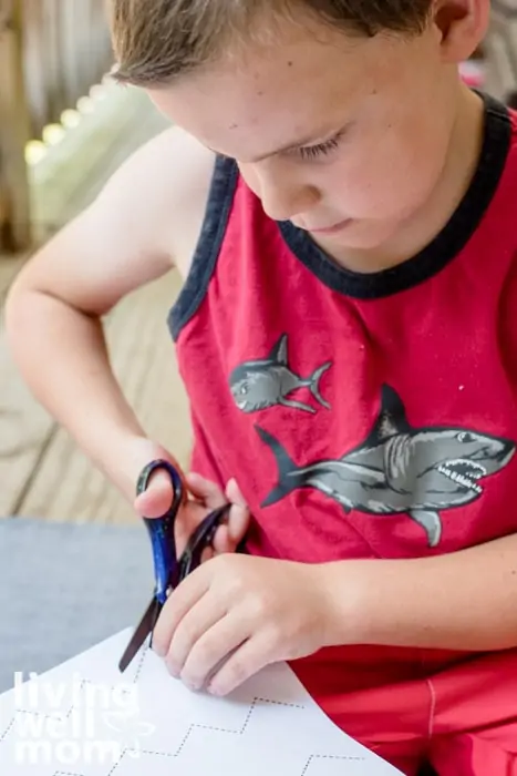 A elementary aged boy practicing scissor skills on a free printable. 