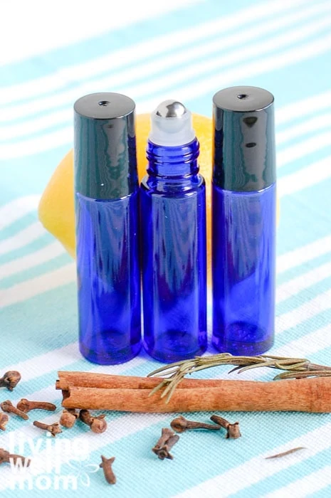 3 essential oil rollers in a row with cinnamon stick and lemon