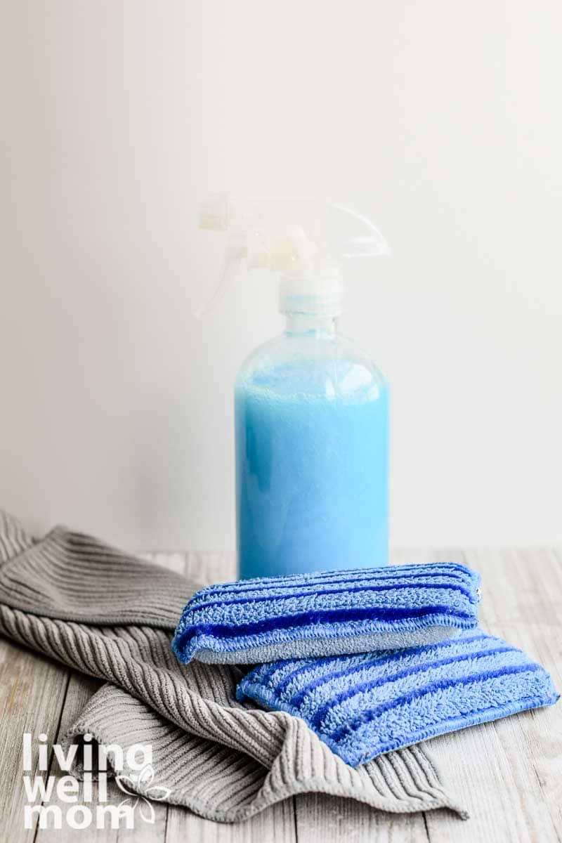 homemade shower cleaner in glass bottle with sponges and cleaning cloths